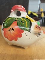 Side view of ceramic hand-painted chicken piggy bank showing red flower and green leaves design.