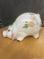 Side view of the white ceramic piggy bank showing floral painting and details of face and feet