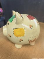 Side view of the cream ceramic piggy bank showing hand-painted patchwork floral details in yellow, red and green.