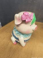 Side angle photo showing the piggy bank's pink bow, blue outfit, and green sticker on head.