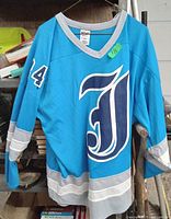 Front and partial side view of blue and grey athletic jersey with number 24 on sleeve and stylized 'J' on the front hanging outdoors