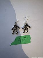 Pair of skeleton-shaped dangling earrings on a white surface with numbered green tape.