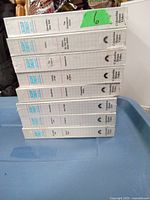 Seven factory sealed Star Trek The Next Generation VHS tapes in white cases stacked horizontally on a blue plastic bin.