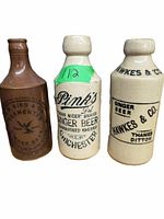 Three vintage ceramic ginger beer bottles shown side by side with clear brands and labels visible.