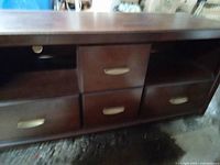 Front view of dark stained wooden TV stand showing four drawers with cream handles and two open shelves.