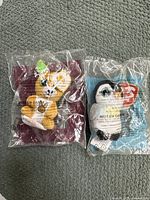 Photo showing two McDonald's plush toys sealed in their original plastic packaging, placed side by side on a grey carpet.