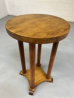 Full view of the wooden side table showing round top and four cylindrical legs attached to square-shaped base with curled feet.