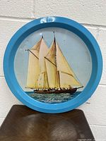 Front view of round blue tin tray showing full ship design with sails and blue rim.