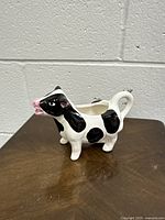 Ceramic Holstein cow-shaped creamer, side view showing black and white spots and pink nose.