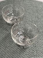Two clear crystal glass bowls with floral etching, shown from an angled top view on a textured surface.