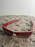 Front view of red plastic rectangular glasses placed on knitted gray surface.