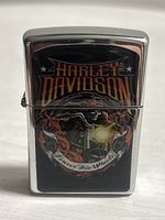 Front view of metal lighter showing detailed Harley Davidson engraving with motorcycle and flames.
