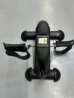 Top view of black compact pedal exercise bike with adjustable foot pedals and digital display showing 3.4.