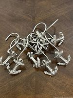 Top view of 10 silver-toned metal anchor-shaped shower curtain hooks spread out on wooden table.