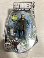 Front view of packaged Men in Black 3 Boris action figure with visible jetpack accessory, showing branding and play features.