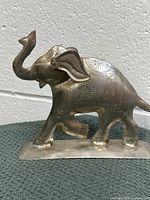 Front side view of metal elephant figurine showing raised trunk, large ears, and engraved detailing on the body.