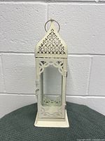 Front view of the cream-colored metal and glass wind lantern showing the hinged door and decorative cutouts.