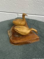 Pair of wooden geese carved and mounted on wooden base viewed from front side, showing two geese positioned with one upright and one leaning forward.