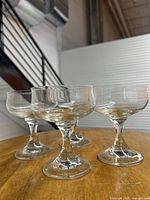 Four clear glass martini glasses displayed on wooden surface showing stems and bowls from side angle.
