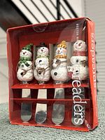 Original red box showing 4 snowman spreaders with ceramic handles in various winter attire, some packaging wear visible