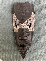 Front view showing intricate carvings and geometric patterns on dark wood mask, highlighting facial features and paint accents.