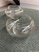 Photo showing two rounded clear glass potpourri vases placed on a textured surface with reflections visible on the glass