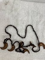 Full view of vintage Hawaiian brown Koa wood and apple seed necklace lei laid on white textured background.