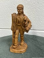 Front view of the hand-carved wooden statue showing facial features, clothing details, rope and container held by the figure.