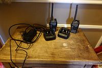 Two handheld radios, two chargers, power adapter on wooden table
