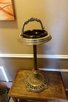 Full view of the ornate cast metal floor ashtray with black glass insert and handle