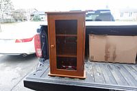 Front view of small wooden display cabinet on truck bed showing glass door, knob and interior shelves