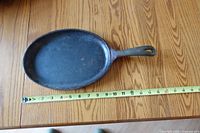Top view of oval cast iron frying pan with measuring tape showing size