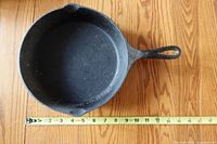 Top view of cast iron frying pan showing interior and pour spouts with measuring tape for scale