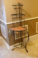 Full view of black wrought iron corner baker's rack with wood shelf insert