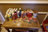 Tabletop view of acrylic paints, ribbon spools, sealed ribbon packs and bead bags