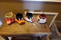 Four plastic Looney Tunes character head cups lined on wooden surface