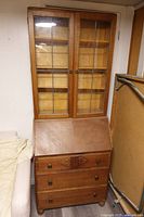 Full view of oak secretary cabinet showing glass-door hutch, drop-front desk, and three drawers