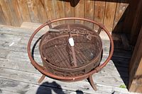 Top view of round steel fire pit showing grate, safety ring, legs, and included poker resting across opening