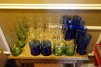 Group of assorted clear, blue and green cylindrical glass vases in two heights displayed on small table
