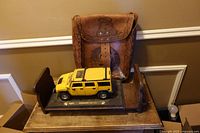 Leather purse hanging behind tabletop with yellow Hummer model and wooden cradle