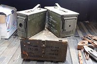Front view of two steel cans on wooden crate showing stencilling and general wear