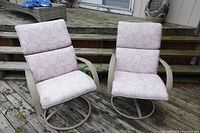 Front view of the two metal patio swivel rocking chairs with cushions on wooden deck