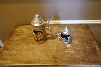 Large and small lidded ceramic beer steins on table