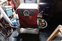 Front view of red stick welder on wheeled cart with cables and gloves