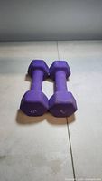 Two purple hex dumbbells placed side by side on a tiled floor, showing the length and side profile.