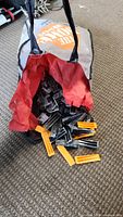 Two bags filled with black and orange plastic tile leveling wedges placed on a carpeted floor, spilling out slightly