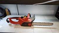 Full profile image of the electric chainsaw showing the body, handle, blade, and chain on a white surface.