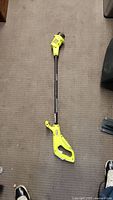 Full view of Ryobi electric weed whacker laid on carpet showing entire length including cutting head and handle.