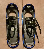 Pair of blue framed Atlas snowshoes with black nylon decking and adjustable straps, showing top view of both snowshoes.
