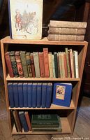 Wooden bookcase filled with various vintage books including a set of blue volumes, books with colorful spines, and larger books on top shelf.